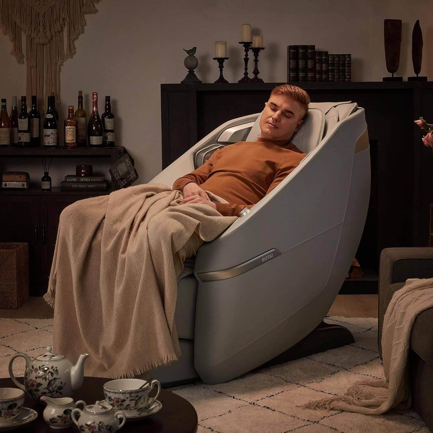 Man relaxing in Ekanite massage chair and sofa in cozy living room with a blanket, showcasing tablet control and foot massager features. best massage chair uae, massage chair Dubai, massage chair uae, massage chair Saudi Arabia, كرسي التدليك, Best massage